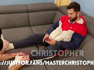 Two slaves lick feet while master plays videogames